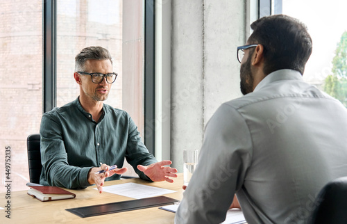 Two diverse business executive partners negotiating at board meeting, manager adviser consulting client discussing financial partnership contract sitting at table in office. Job interview concept. photo