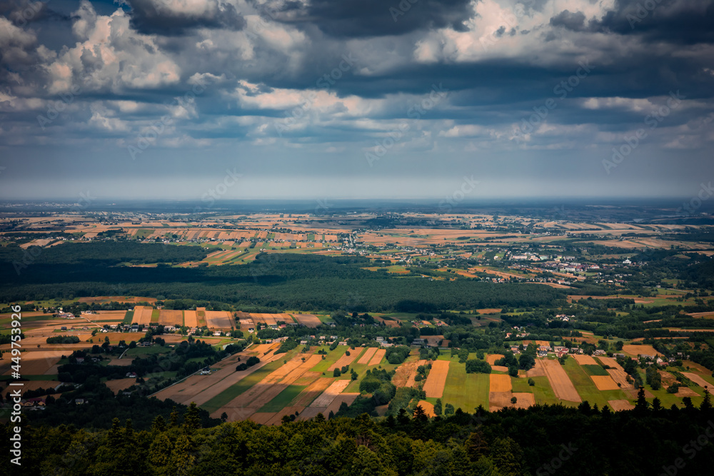A picturesque panorama from Swiety Krzyz in Swietokrzyskie Mountains, Poland. 
Cloudy sky. Golden fields, forest and mountains in background. 
