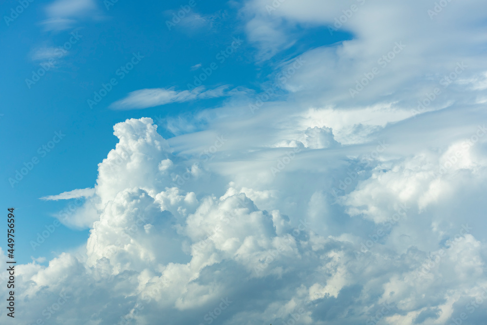 Fototapeta premium Towering form of cumulonimbus rain cloud contrasted against a vibrant blue sky rising up and lit up from below. Weather conditions and climate detail background.