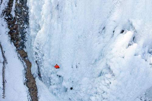 Aerial shot of an ice slope bumps, ridges, and icicles by which climbing up man using traction ice tool technique © 24K-Production