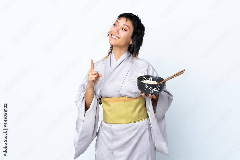 Young woman wearing kimono holding a bowl of noodles over isolated white background intending to realizes the solution while lifting a finger up Young woman wearing kimono holding a bowl of noodles over isolated white background intending to realizes the solution while lifting a finger up