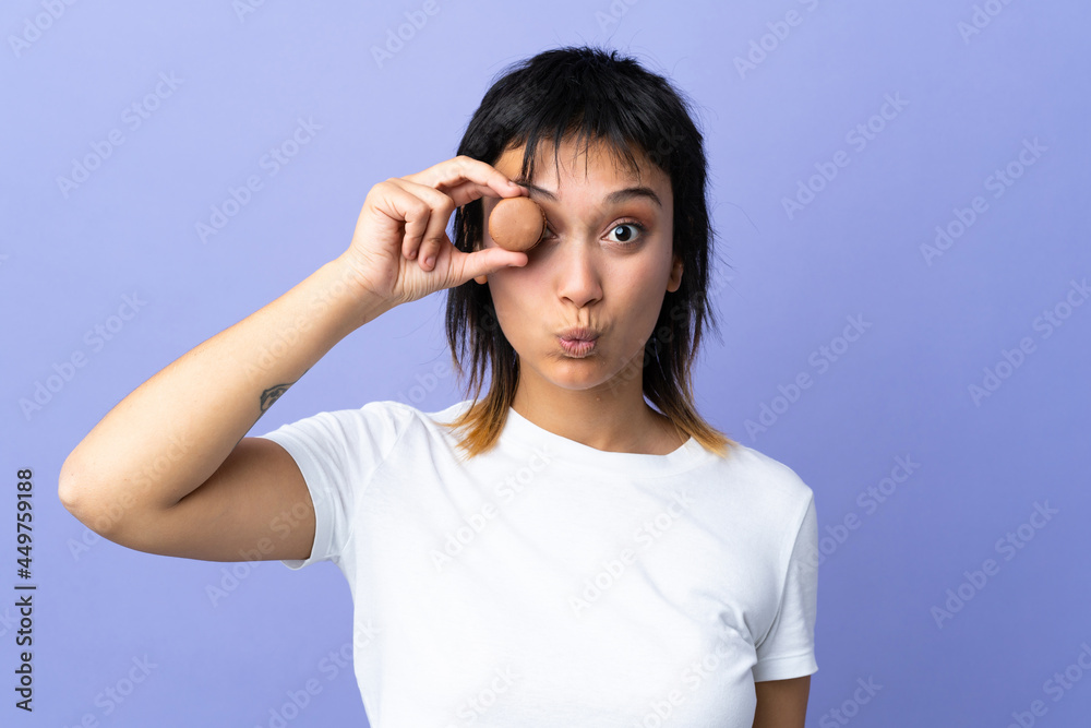 Young Uruguayan woman over isolated purple background holding colorful French macarons with funny face Young Uruguayan woman over isolated purple background holding colorful French macarons with funny face