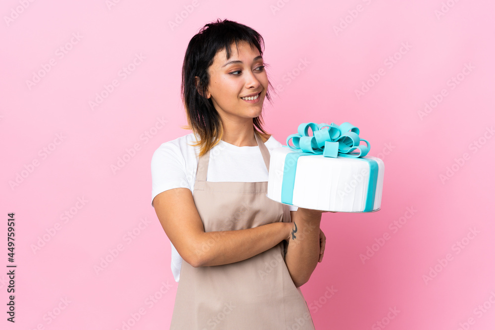 Uruguayan Pastry chef holding a big cake over isolated pink background looking to the side Uruguayan Pastry chef holding a big cake over isolated pink background looking to the side