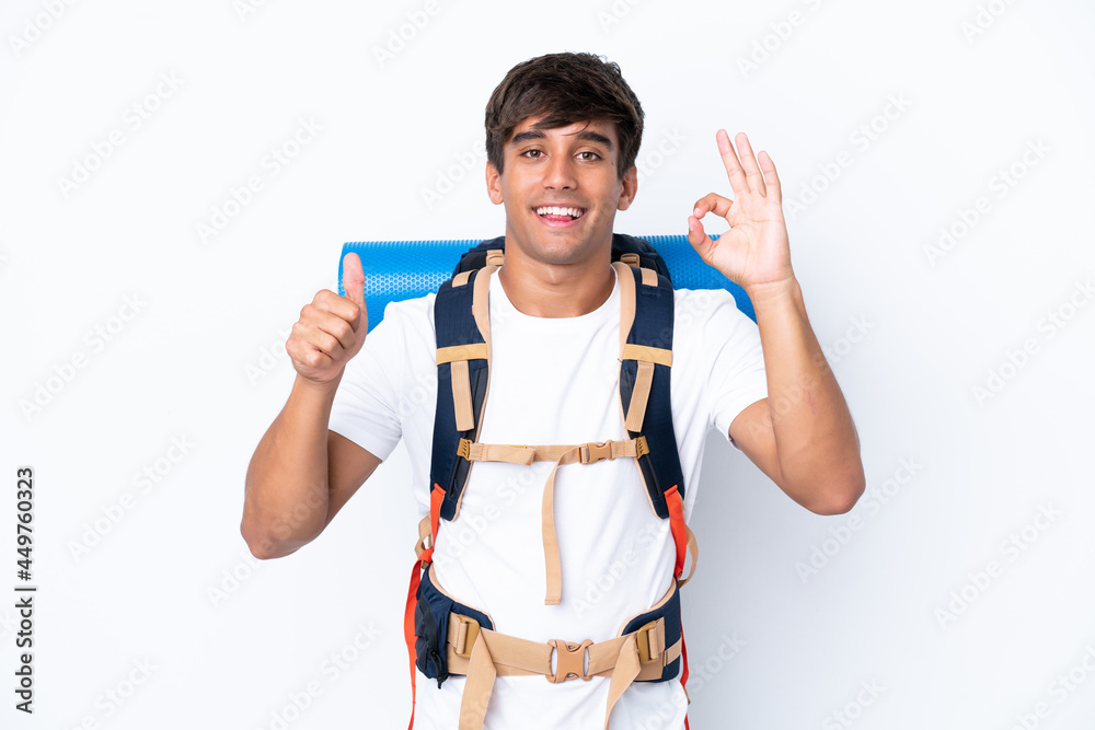 Young mountaineer woman with a big backpack over isolated white background showing ok sign and thumb up gesture