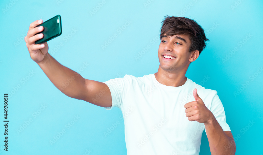 Young caucasian man isolated on blue background making a selfie with mobile phone Young caucasian man isolated on blue background making a selfie with mobile phone