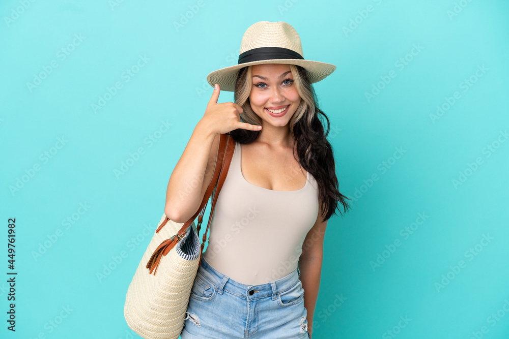Teenager Russian girl with pamel and beach bag isolated on blue background making phone gesture. Call me back sign Teenager Russian girl with pamel and beach bag isolated on blue background making phone gesture. Call me back sign
