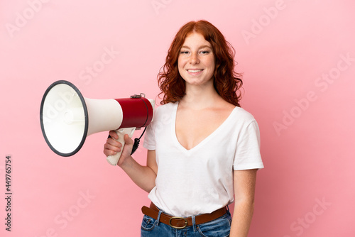 Teenager reddish woman isolated on pink background holding a megaphone and smiling a lot
