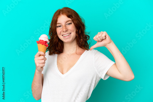 Teenager reddish woman with a cornet ice cream isolated on blue background proud and self-satisfied