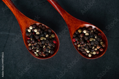 Wooden spoon with a mix of pepper on black background. Dried aromatic spice.
