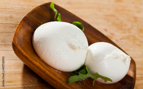Italian artisan cow milk cheese burrata with solid outer shell and creamy texture inside served on wooden plate with arugula