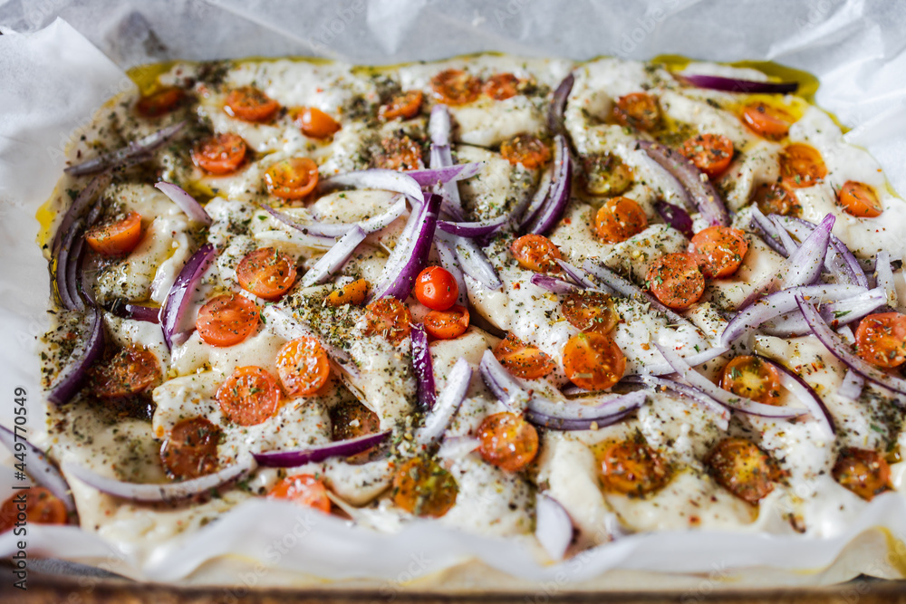 vegan homemade focaccia bread with cherry tomatoes and onions before being cooked, healthy plant-based food