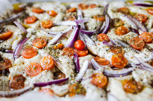 vegan homemade focaccia bread with cherry tomatoes and onions before being cooked, healthy plant-based food