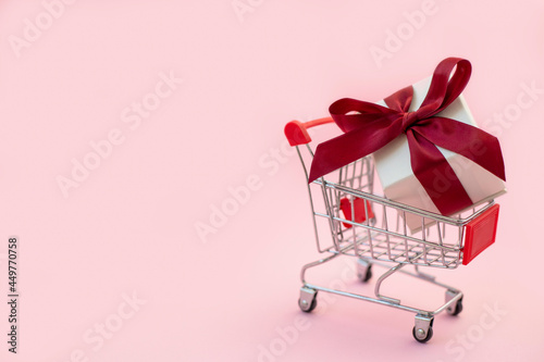 Shopping cart with white gift box and red bow. Holiday shopping concept