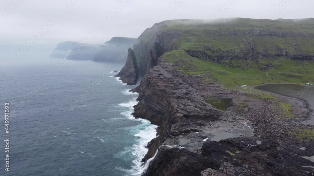 Ocean Waves Hit Grey and Green Cliffs with Waterfall Aerial