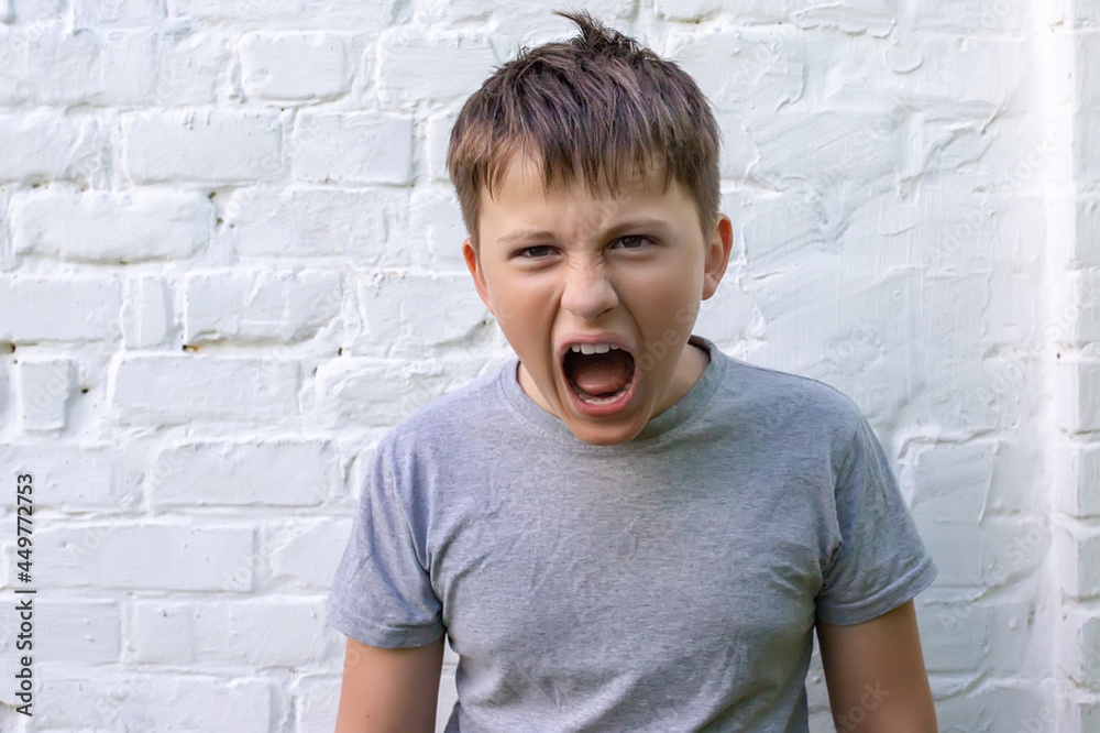 screaming Angry boy teenager with his mouth wide open and squinted eyes against the background of a white brick stubble screaming Angry boy teenager with his mouth wide open and squinted eyes against the background of a white brick stubble