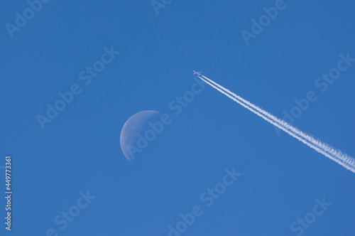Airplane leaving contrails against blue sky with waning moon photo