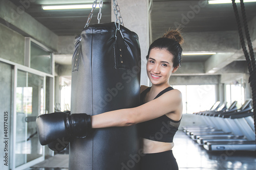 Bilde på lerret Beautiful asian woman wears boxing gloves hugging a sandbag and smile in gym or