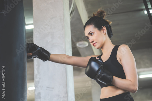 Beautiful asian woman wears boxing gloves knock sandbag in gym or sport center © Mrzproducer