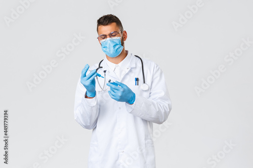 Covid-19, healthcare workers, pandemic and preventing virus concept. Serious doctor in medical mask and gloves, male physician insert coronavirus vaccine from ampoule to syringe