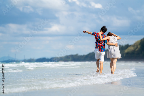 Happy Asian people on beach travel vacation. Young couple holding hand and walking together on the beach in summer sunny day. Boyfriend and girlfriend enjoy and having fun outdoor lifestyle activity.