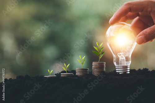 Fotografia alternative energy, Renewable Energy, saving energy and finance, energy stock investment, tree growing up on coin and lightbulb on soil