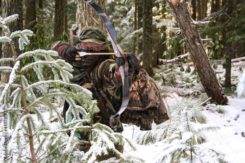 traditional bowhunter ready to shoot in snowy woods photo