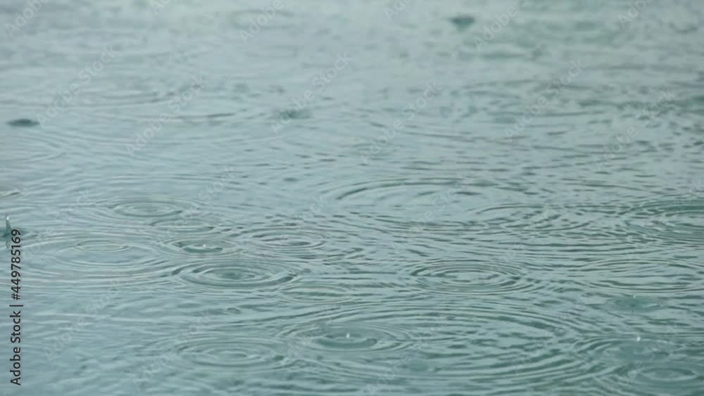 Super slow motion shot of raindrops falling on a quite water surface creating rings Super slow motion shot of raindrops falling on a quite water surface creating rings