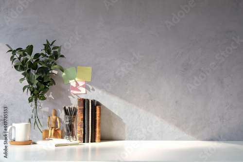 Books, coffee cup, notebook and potted plant on white table with concrete wall. Copy space.