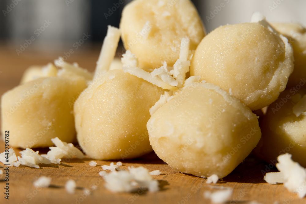 Gnocchi pasta pre-cooked on a wooden board with grated cheese and basil. Macro close up. Selective focus.