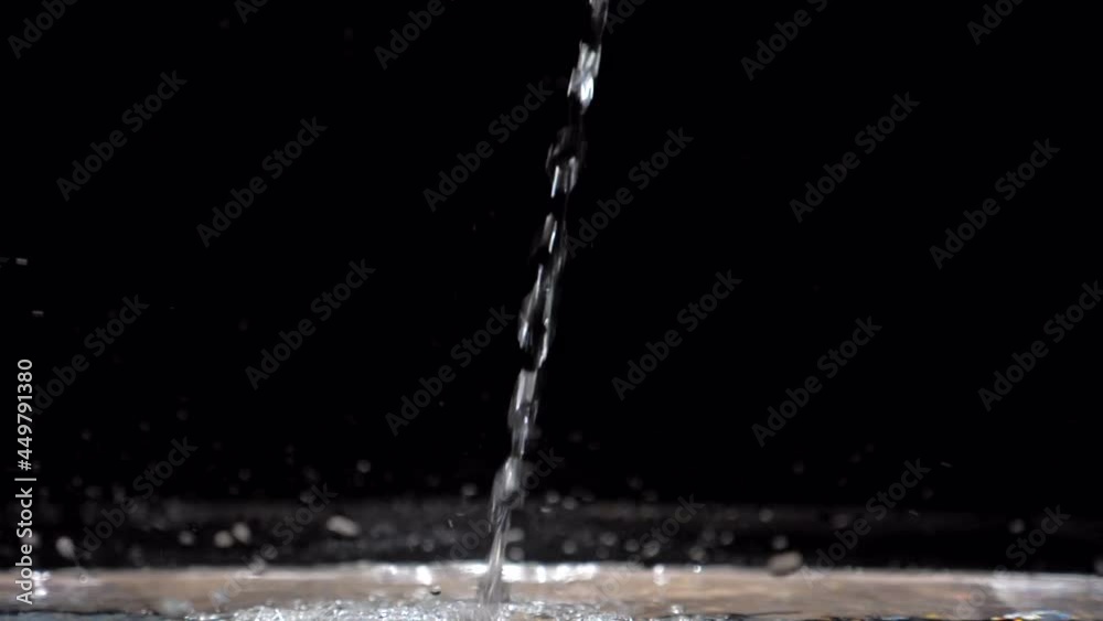 Slow motion stream of water drops down in aquarium on a black background. Slowmotion crystal clear water flow hits the surface