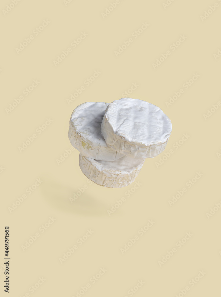 Three wheels of Camembert cheese with white noble mold on pastel yellow background. Food levitation.