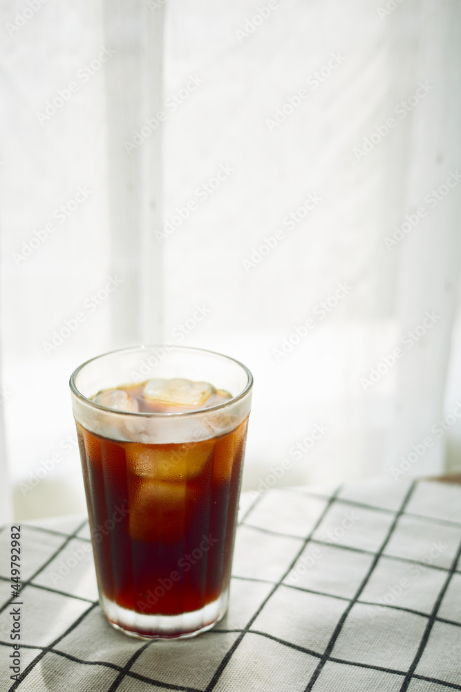 Cold brew cofee with ice on checked cloth beside a window with white curtain Cold brew cofee with ice on checked cloth beside a window with white curtain