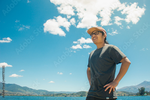 Young latin men looking at the lake with a dominant position. A confident Man in a beauty blue sky located in a lake from ecuador. Theres a horizon with trees and mountains.