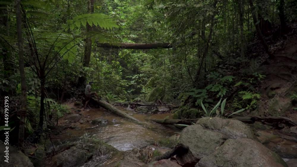 Male traveler hiker looking around exploring mountain river stream with hiking flashlight in jungle. Beautiful dense foliage, flowing creek scene in tropical rainforest. Adventures and extreme tourism Male traveler hiker looking around exploring mountain river stream with hiking flashlight in jungle. Beautiful dense foliage, flowing creek scene in tropical rainforest. Adventures and extreme tourism