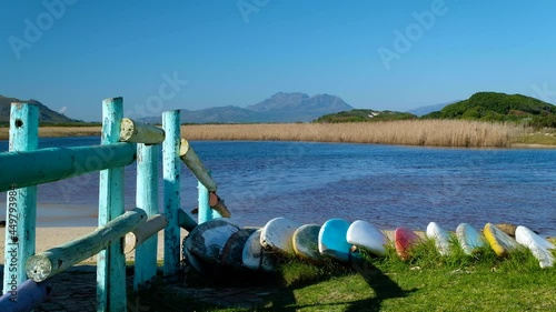 Paddle skis stacked on shore next to beautiful lagoon, popular holiday destination, reeds and mountain background photo