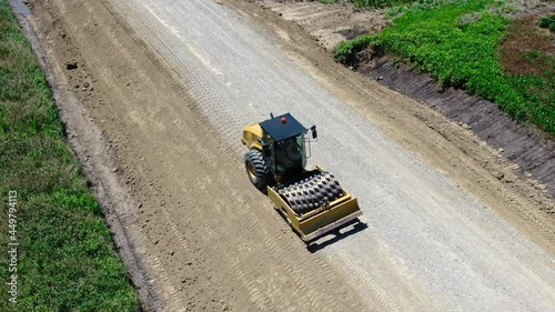 Aerial high angle footage of Sheepsfoot roller compressing new road in rural US. Drone. photo