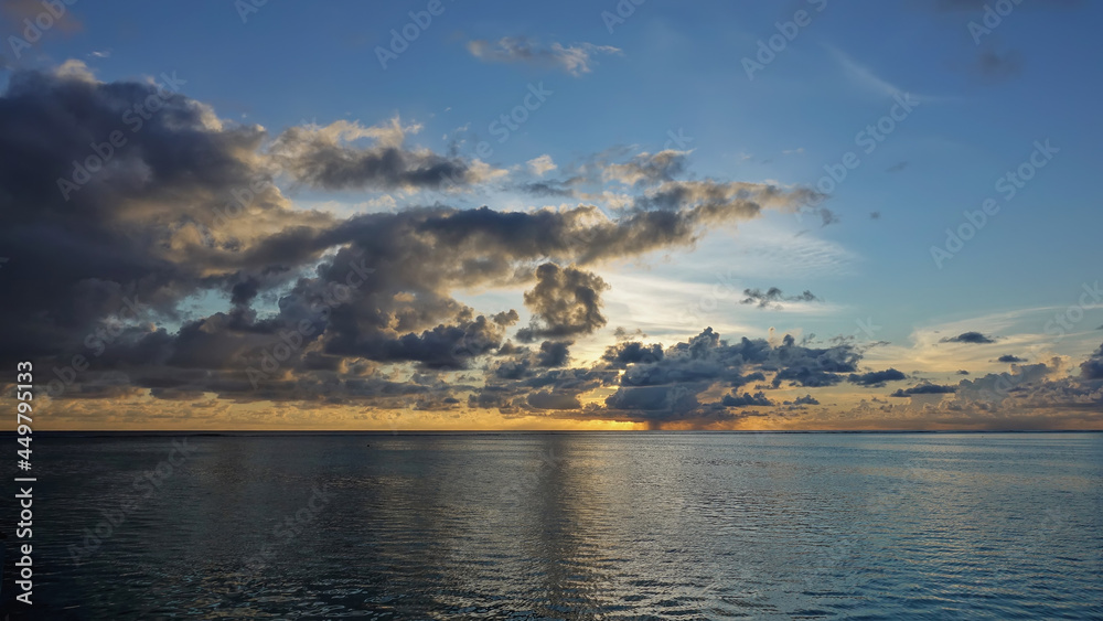 Sunset sky and ocean. The sun has set. Purple clouds are highlighted in orange. Reflection on calm water. Maldives