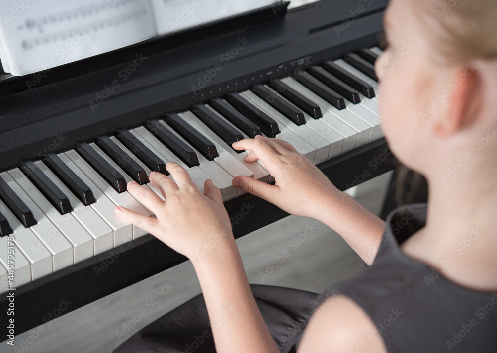 Fototapeta premium a girl in a gray dress plays an electronic piano on a music book . Home Schooling Close up