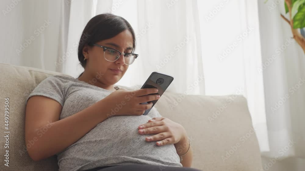 a pregnant latinx woman texting on her phone a pregnant latinx woman texting on her phone
