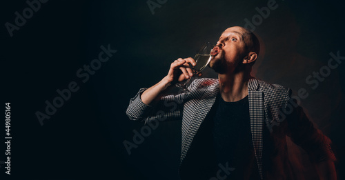Night club party. Drunk man. Holiday joy. Festive celebration. Silly hipster guy in casual jacket drinking glass of champagne isolated black long exposure defocused light copy space.
