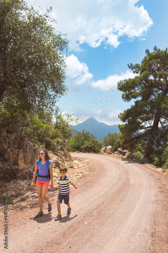A woman with a backpack walks with her son on a mountain road.