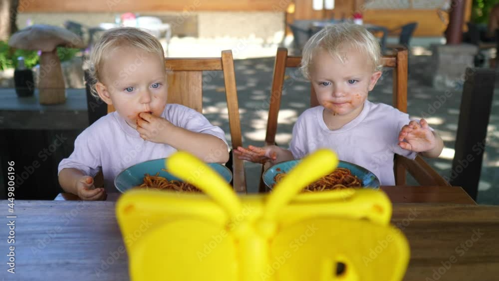 Twin sisters learning to feed themselves with their hands developing motor skills. Lunch outdoors 