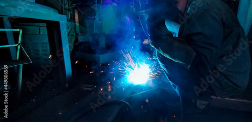 Welder welding metal with argon arc welding machine and has welding sparks. A man wears welding mask and protective gloves. Safety in industrial workplace. Welder working with safety. Steel industry.