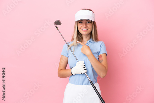 Young golfer player woman isolated on pink background pointing to the side to present a product