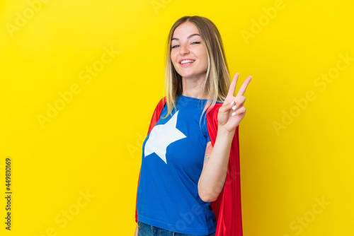 Super Hero Romanian woman isolated on yellow background smiling and showing victory sign