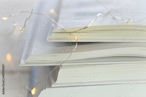 Reading of books. Books with white covers stack close-up and garland on blurred blue background.Literature and hobby. Winter books. Winter cozy reading.books close up. High quality photo