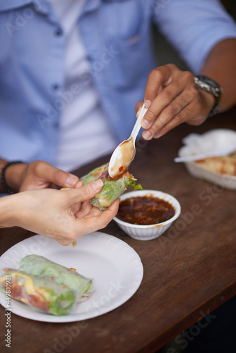 Young man putting spoon of hot sauce on spring roll in hand of his girlfriend