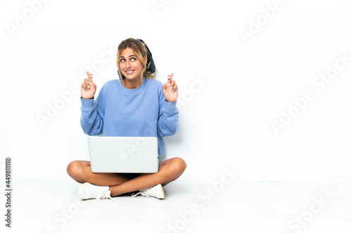 Young blonde Uruguayan girl with the laptop isolated on white background with fingers crossing © luismolinero