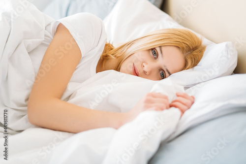 Morning relaxation. Rest wellness. Sleep pleasure. Home weekend. Peaceful happy young pretty woman under blanket in soft clean white bed sheets enjoying pleasant cozy bedroom.