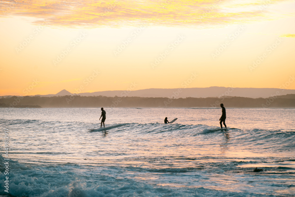 Silhouette of Surfers Riding a Wave at Sunset Time in Noosa,Queensland,Australia